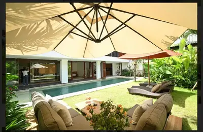 a pool with chairs and umbrellas next to a house at Tatkala Villa Seminyak in Seminyak