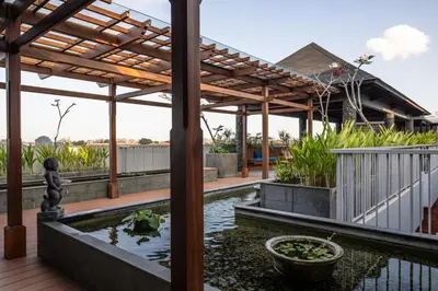 a patio with a pond and a wooden pergola at Aralea Coliving in Denpasar