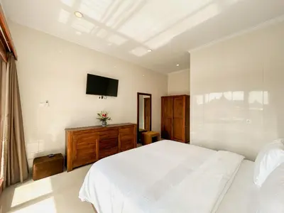 a bedroom with a white bed and a television at James Guest House in Seminyak