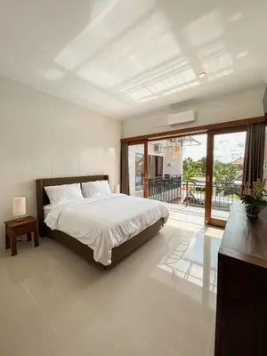 a white bedroom with a bed and a balcony at James Guest House in Seminyak