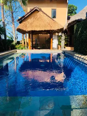 a large swimming pool with a straw hut next to a house at Giri's Villa Jimbaran in Jimbaran
