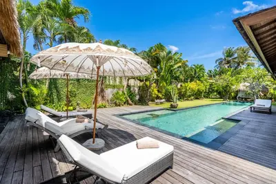 an outdoor deck with chairs and an umbrella next to a swimming pool at Villa Ku Besar by Villa Finder in Dalung