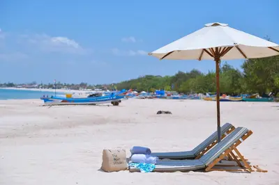 a beach chair with an umbrella and a bag on a beach at The Open House Jimbaran Bali in Jimbaran