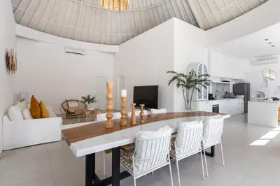 a living room with a large wooden table and white chairs at Villa Weiss Berawa in Canggu