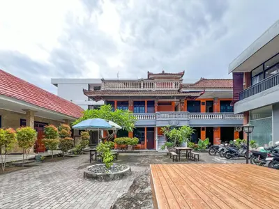 a courtyard of a building with tables and an umbrella at RedDoorz at Mahendra Beach Inn Kuta in Kuta