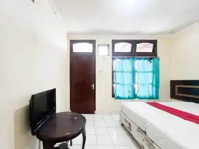 a bedroom with a bed and a tv and a table at RedDoorz at Mahendra Beach Inn Kuta in Kuta
