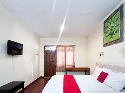 a bedroom with a white bed and a tv at RedDoorz at Mahendra Beach Inn Kuta in Kuta