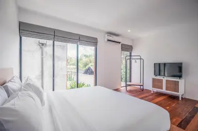 a white bedroom with a large bed and a tv at Umalas Living Villa in Canggu