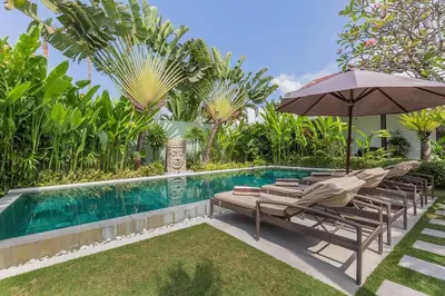 a swimming pool with lounge chairs and an umbrella next to a pool at Villa Budha 2 4bedrs 12m Pool, 700m2 garden&BBQ, central & quiet in Seminyak