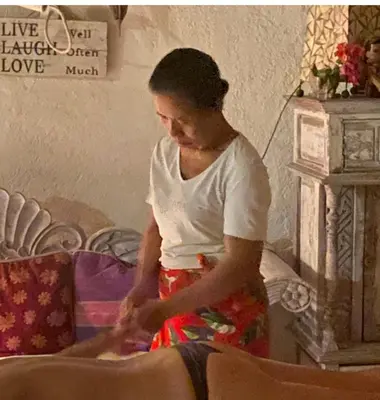 a woman in a white shirt standing next to a bed at Shady Grove Healing Centre & Homestay w house rules please read before booking in Sanur