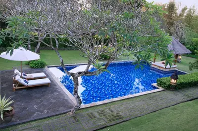 a pool with a tree and two chairs and an umbrella at Villa Hanani in Jimbaran