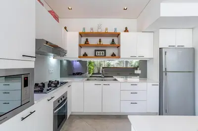 a white kitchen with white cabinets and a refrigerator at Villa Ace - Modern 2BR Villa in Seminyak with Spacious Bedrooms, Bathtub & Private Pool in Seminyak
