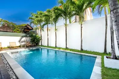 a pool with palm trees in front of a white wall at Villa Oberoi in Seminyak