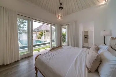 a white bedroom with a large bed and a pool at Beachside Colonial Elegance: 4BR in Canggu in Canggu