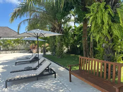 a group of benches with an umbrella and trees at Three-Bedroom Pool Villa at Anwa Residences in Canggu