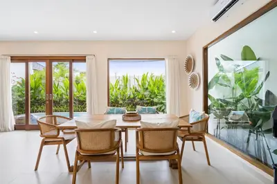 a dining room with a table and chairs and a large window at Roselle Villa by Betterplace in Canggu
