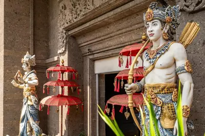 two statues in front of a building with red umbrellas at Ammara Legian By Vilarisi - 8 Minute Walk To The Beach in Legian