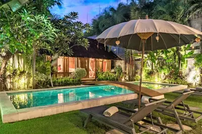 an umbrella and chairs next to a swimming pool at Villa Joglo Oberoi Seminyak Beautiful 4BR Villa Prime Location in Seminyak