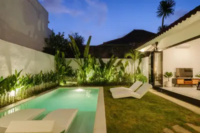 a backyard with a swimming pool and two white chairs at Villa Marina Seminyak in Seminyak