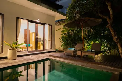 a pool with two chairs and an umbrella next to a house at Nossa Casa Villa in Seminyak