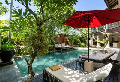 a pool with a red umbrella and some chairs and a table at Villa Pulung Jimbaran by Nakula in Jimbaran