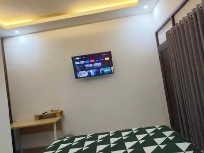 a room with a bed and a tv on the wall at Justin Guest House in Jimbaran