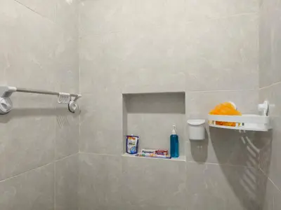 a bathroom with a tiled shower with a shelf at Justin Guest House in Jimbaran