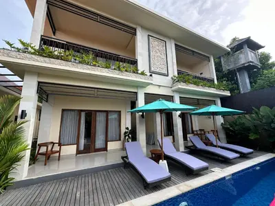a house with chairs and umbrellas next to a pool at Villa Kumaru Luxury 4BR inc breakfast and airport pickup in Canggu