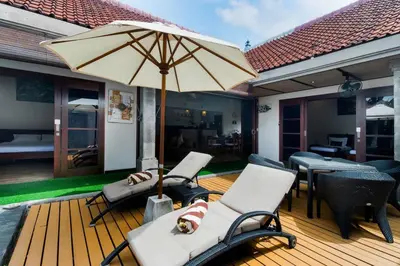 a wooden deck with chairs and an umbrella at Villa Tranquil Holiday Villa in Seminyak