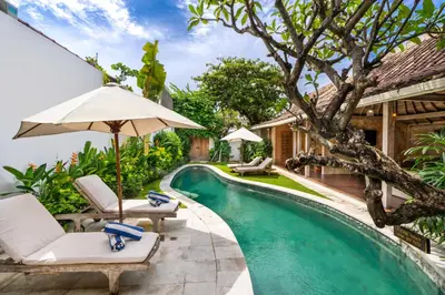a pool with chairs and an umbrella next to a house at Villa Amsa by Pertama Management in Seminyak