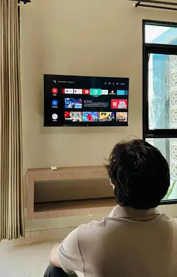 a woman sitting in front of a tv in a living room at Nawasena Room Suite in Sanur