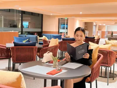 a woman sitting at a table holding a book at voco Bali Seminyak by IHG in Seminyak