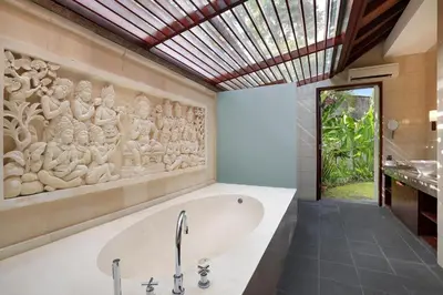 a bath tub in a bathroom with a wall art at Barimantra 4BR Trees View Pool Villa CYN in Jimbaran