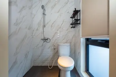 a bathroom with a toilet and a marble wall at Cove Tripuri House Bali in Denpasar