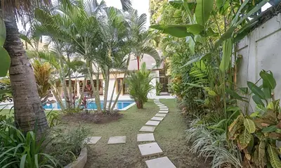 a resort yard with a swimming pool and palm trees at Villa Umah Maya 3BR Seminyak in Seminyak