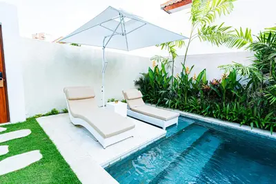 a pair of chairs and an umbrella next to a swimming pool at La Boutique Lux's Villas Seminyak Bali in Seminyak