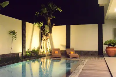 a swimming pool with two chairs and a palm tree at The Arnaya in Kuta