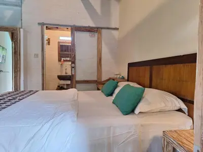 a bedroom with a white bed with two green pillows at Oma Joglo Jimbaran in Jimbaran