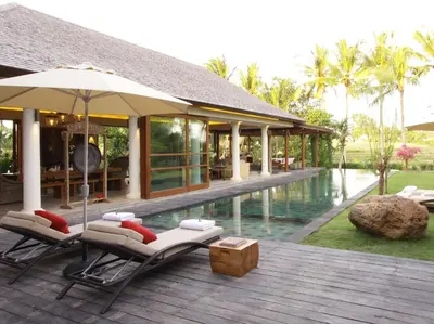 a deck with chairs and an umbrella next to a pool at Dea Villas in Canggu
