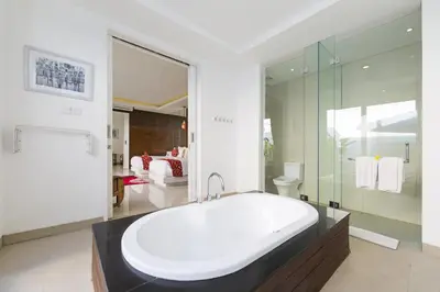 a bathroom with a large white tub and a bedroom at Bajra Bali Villa Seminyak in Seminyak