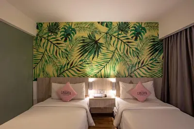 two beds in a room with a mural of palm trees at Liberta Seminyak Hotel in Seminyak