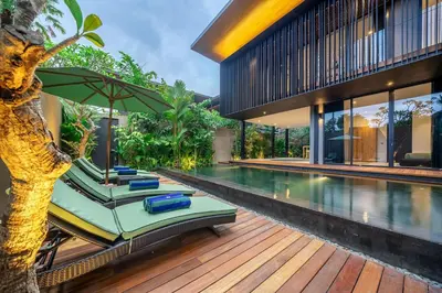 a pool with lounge chairs and an umbrella next to a house at The Continental Modern Luxury 4 BR Villa in Seminyak Central in Seminyak