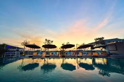 a swimming pool with umbrellas and chairs and the sunset at Damarlangit 1 BR Superior Terrace in Seminyak