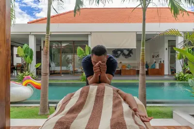 a man sitting on a blanket in front of a pool at Villa Marlex by Bukit Vista in Seminyak