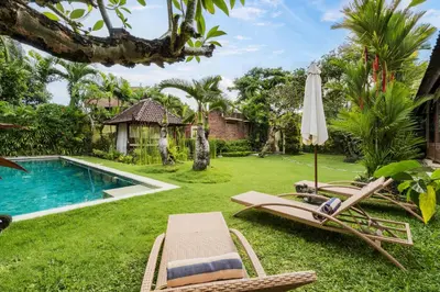 a yard with chairs and an umbrella and a swimming pool at Villa Kuda Sumba by BaliSuperHost in Kerobokan
