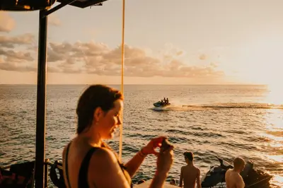a woman sitting on a beach with a boat in the ocean at Floating Hotel SALTWATER COWBOYS in Kuta