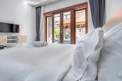 a bedroom with a large white bed and a window at Dukuh Segara Guest House in Legian