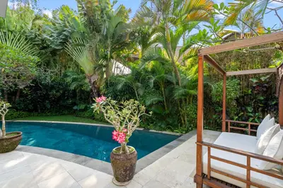 a patio with a bed and a pool with palm trees at Sahaja Villa by Betterplace in Canggu
