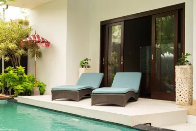 two chairs next to a swimming pool next to a house at Balinese stile villa in Nusa Dua