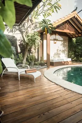 a wooden deck with two chairs and a swimming pool at Segara Beach House Villa - Kuta in Kuta